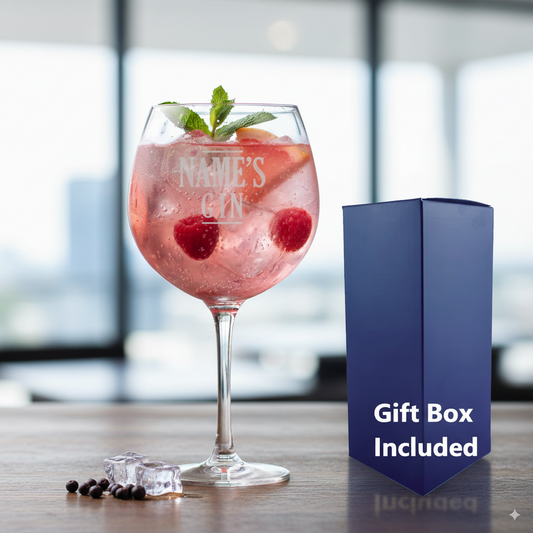 Pink gin cocktail in a  personalised glass with raspberries and mint, next to a blue gift box on a wooden surface.